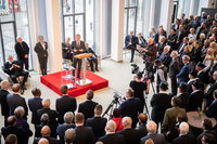 Präsident Imhoff steht auf einem Podest im Festsaal am Rednerpult. Rund um ihn herum stehen mehrere hundert Menschen und hören ihm zu.