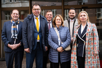 Ein Gruppenfoto aller Teilnehmer:innen vor dem Eingang zum Restaurant. Alle gucken freundlich in die Kamera. Der Botschafter steht in der Mitte.
