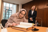 Nadjet Hamdi sitzt am Tisch und trägt sich in das Gästebuch ein. Seitlich versetzt hinter ihr steht Frau Grotheer und sieht ihr dabei zu.