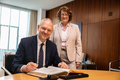 Der Botschafter sitzt am Konferenztisch im Präsidentinnenzimmer und trägt sich in das vor ihm liegende Gästebuch ein. Antje Grotheer steht neben ihm. Beide gucken freundlich in die Kamera.