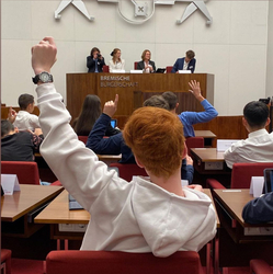 im Vordergrund Schüler:innen, die per Handzeichen abstimmen; im Hintergrund das Präsidium mit Präsidentin Grotheer und Teamer:innen