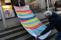 Präsident Imhoff und Hermann Kuhn stehen auf den Stufen vor der Bürgerschaft. Sie falten die Flagge auseinander und halten sie zwischen sich.